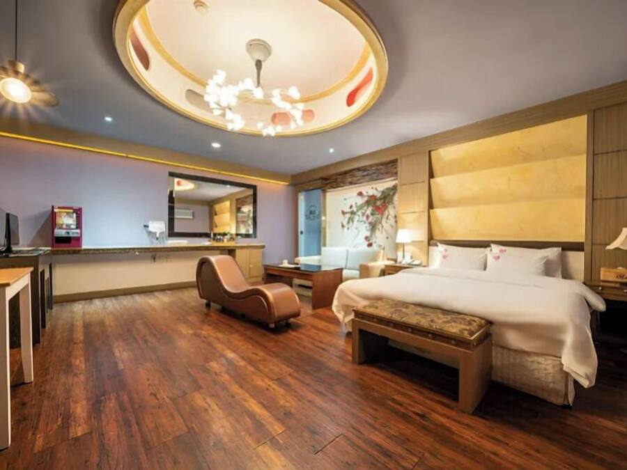 A hotel room with a large bed, a desk, a chair, a small table, and a ceiling light fixture.