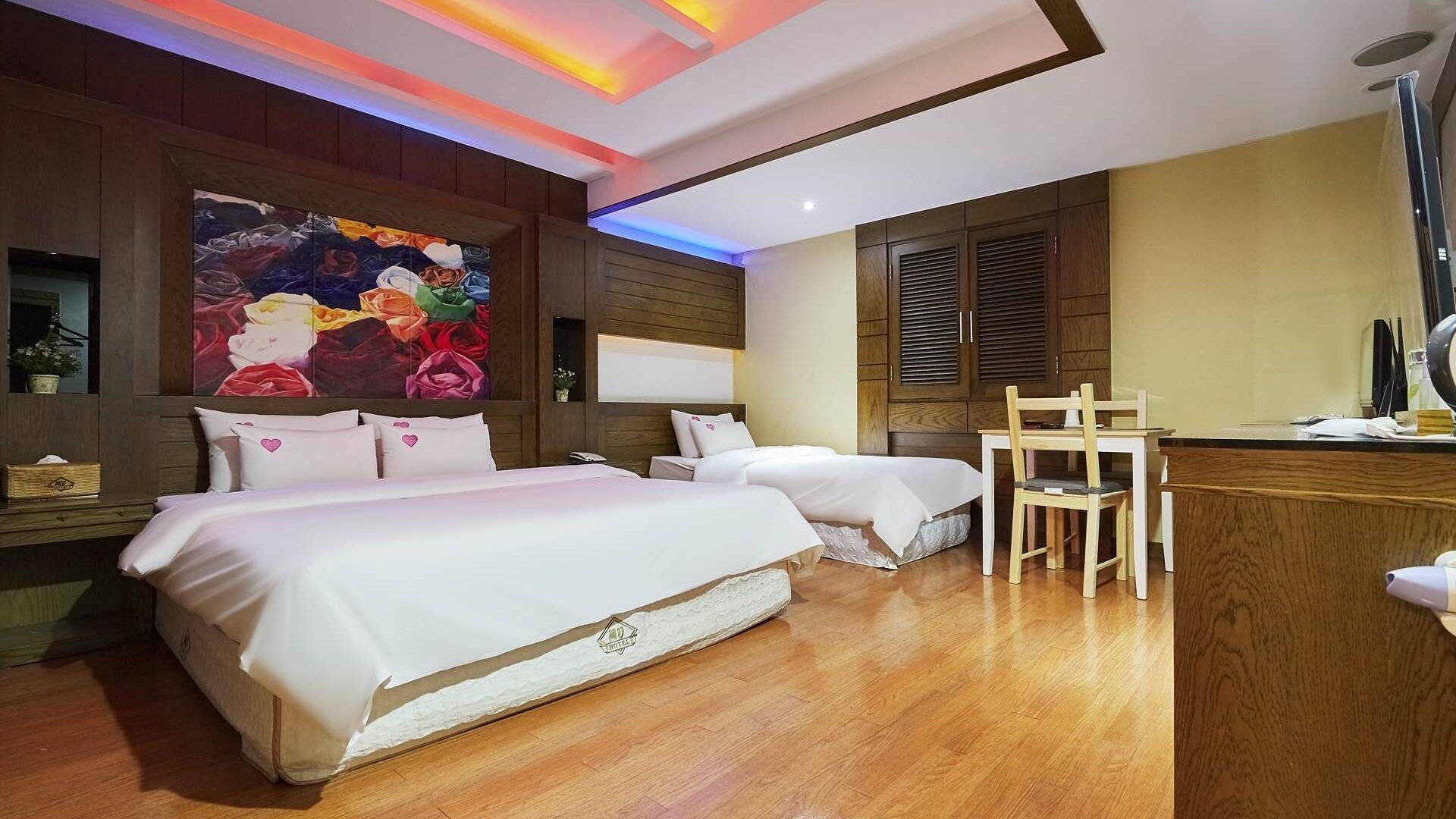 Habitación de hotel con dos camas, un escritorio y un cuadro grande con motivos florales en la pared.