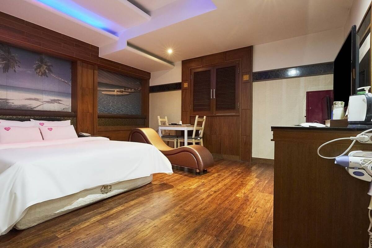 A hotel room with a bed, a desk, a chair, and a painting of a beach scene.