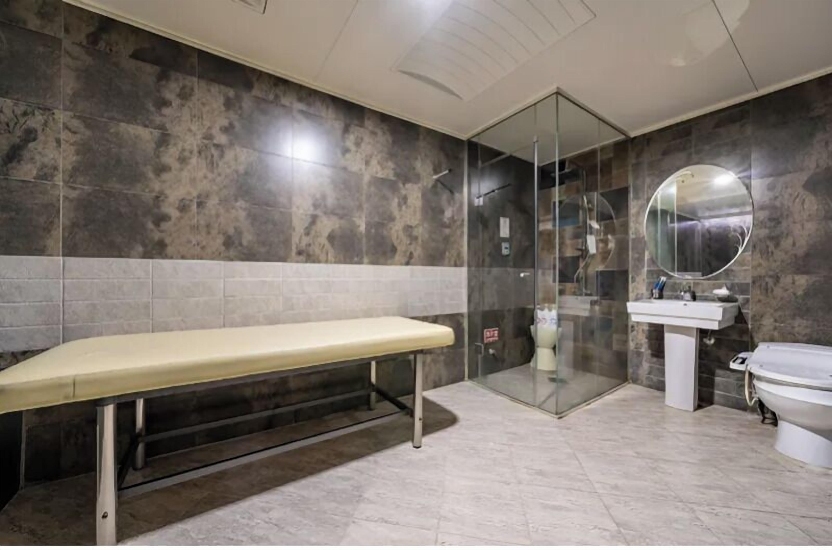 A modern bathroom with a bench, a glass shower enclosure, a sink, and a toilet.