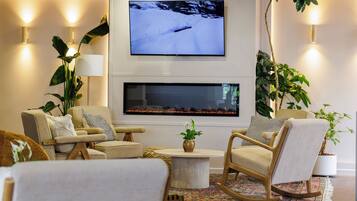 Uma sala de estar moderna com uma TV de tela plana na parede, lareira abaixo, assentos confortáveis e plantas decorativas.