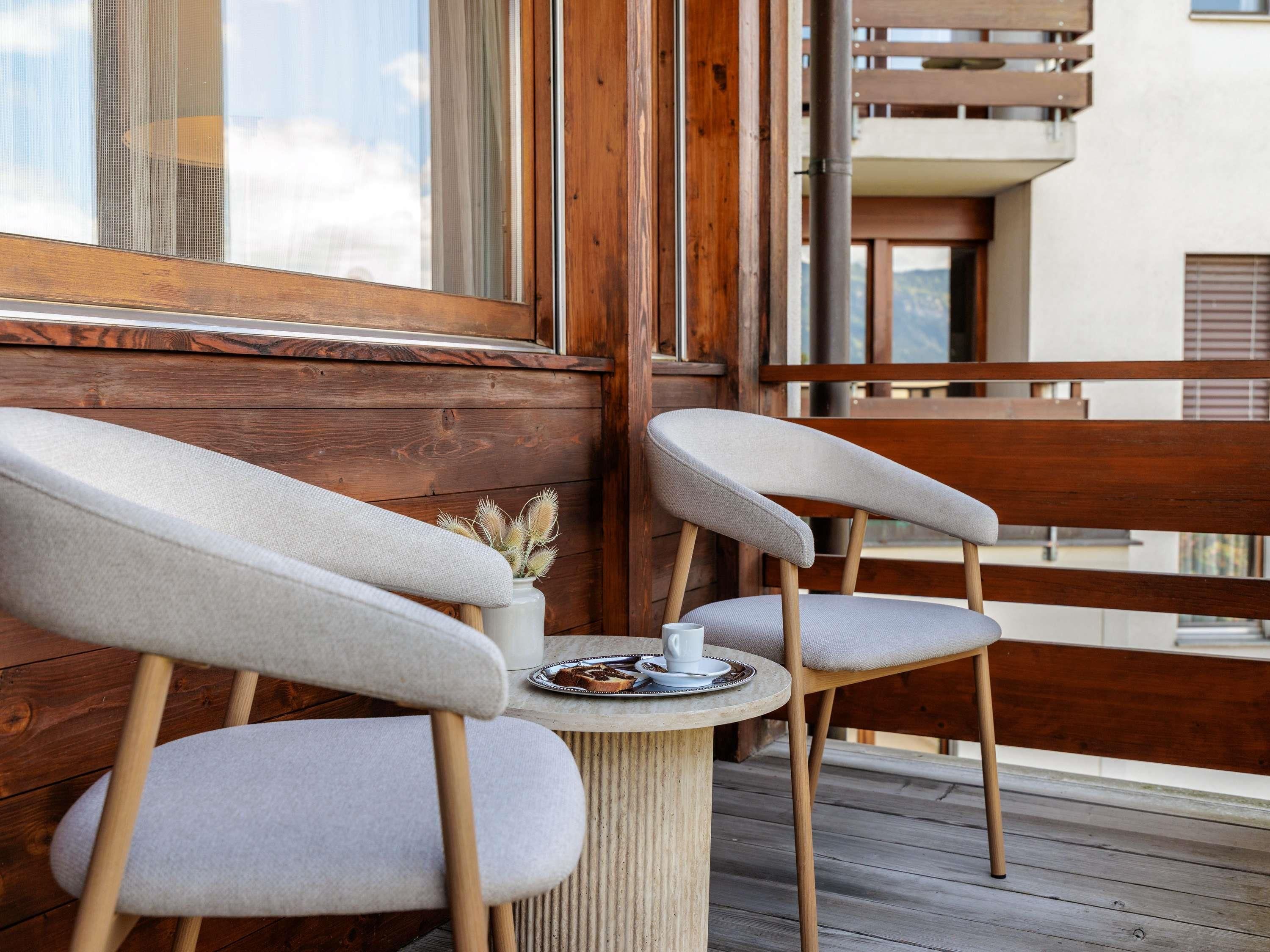 Twee stoelen bij een ronde tafel op een houten terras, met uitzicht op een gebouw met balkons.