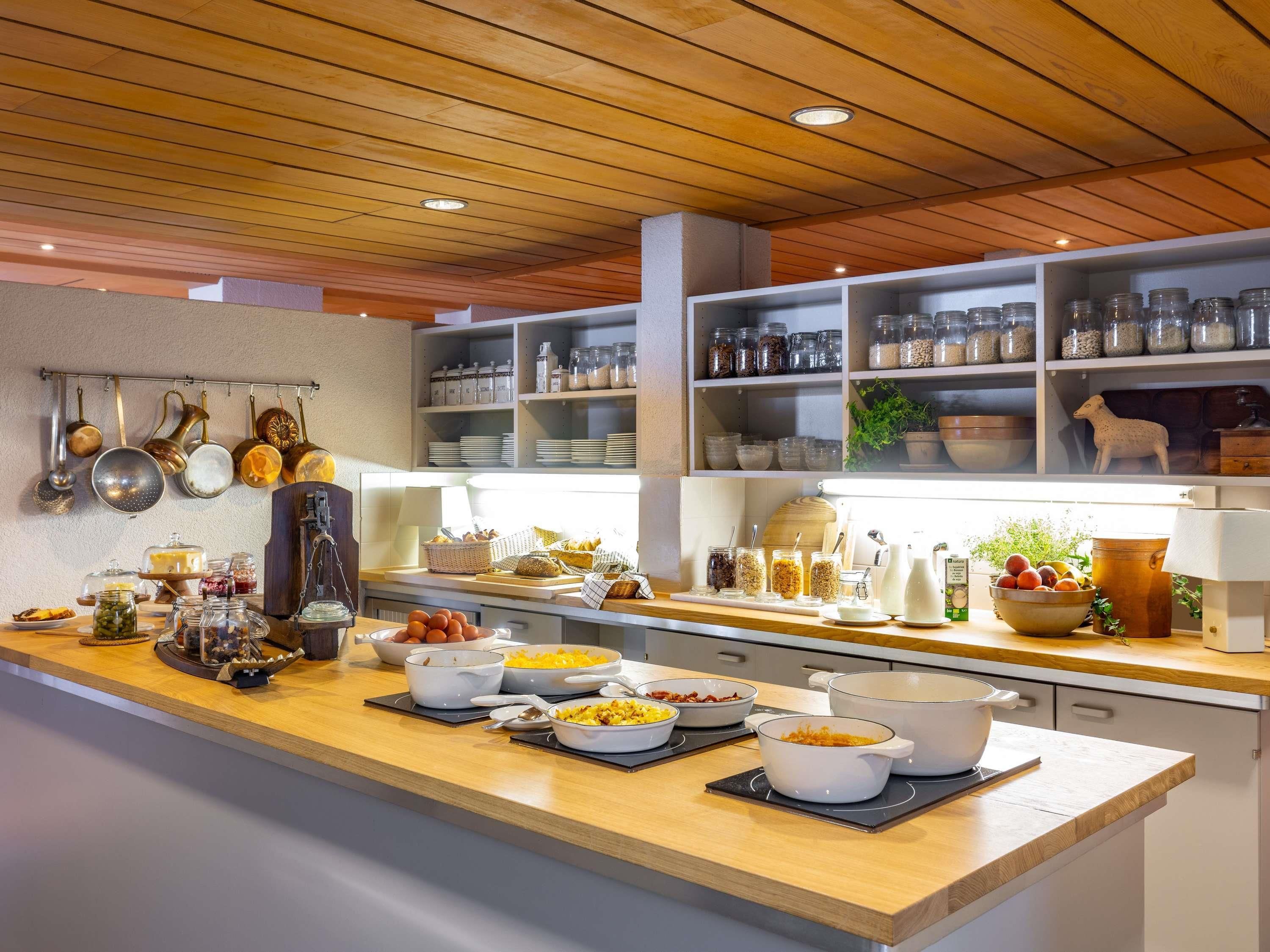 Een keuken met houten aanrechtbladen, hangende pannen en planken met potten en keukengerei.