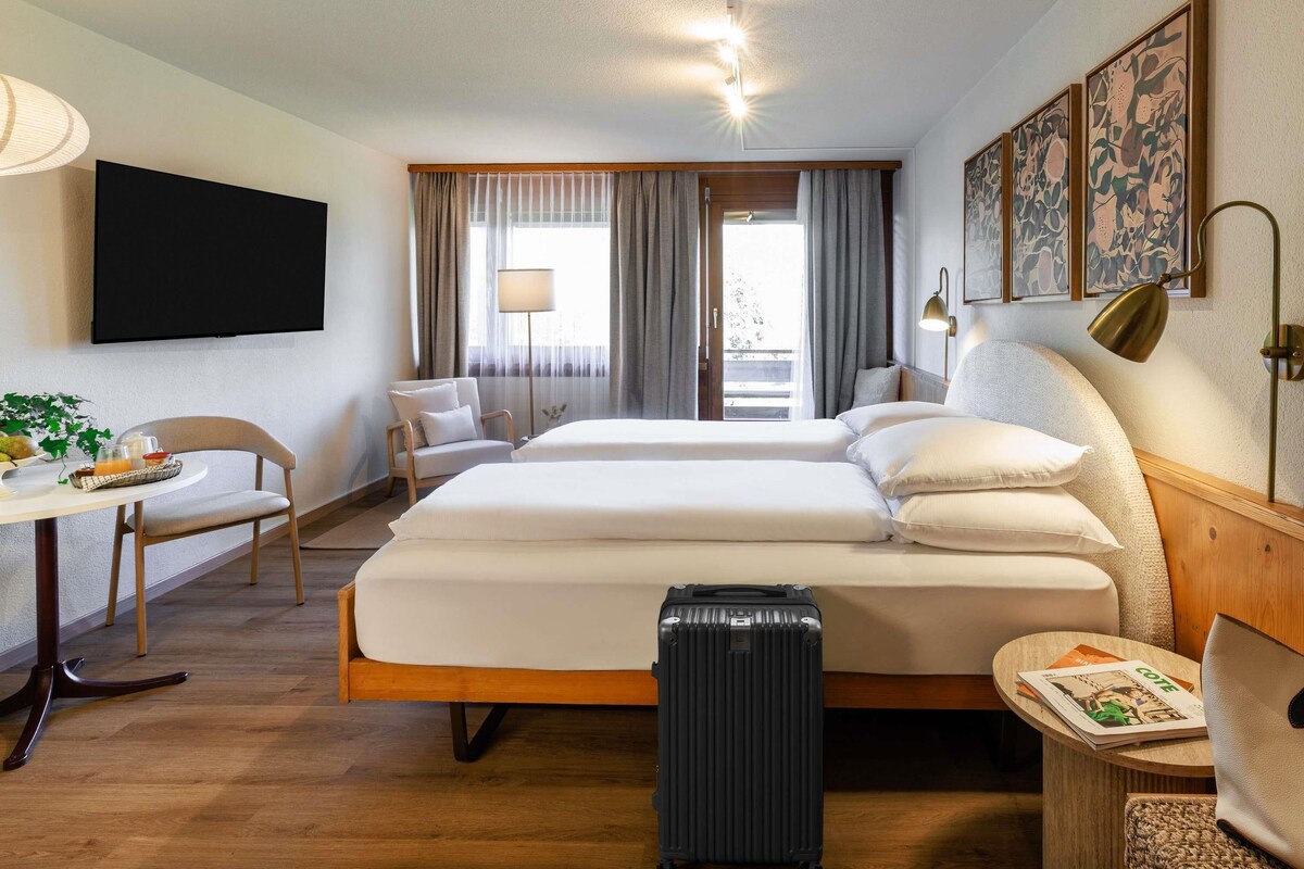 A hotel room with a bed, a desk, a chair, a suitcase, and a TV.
