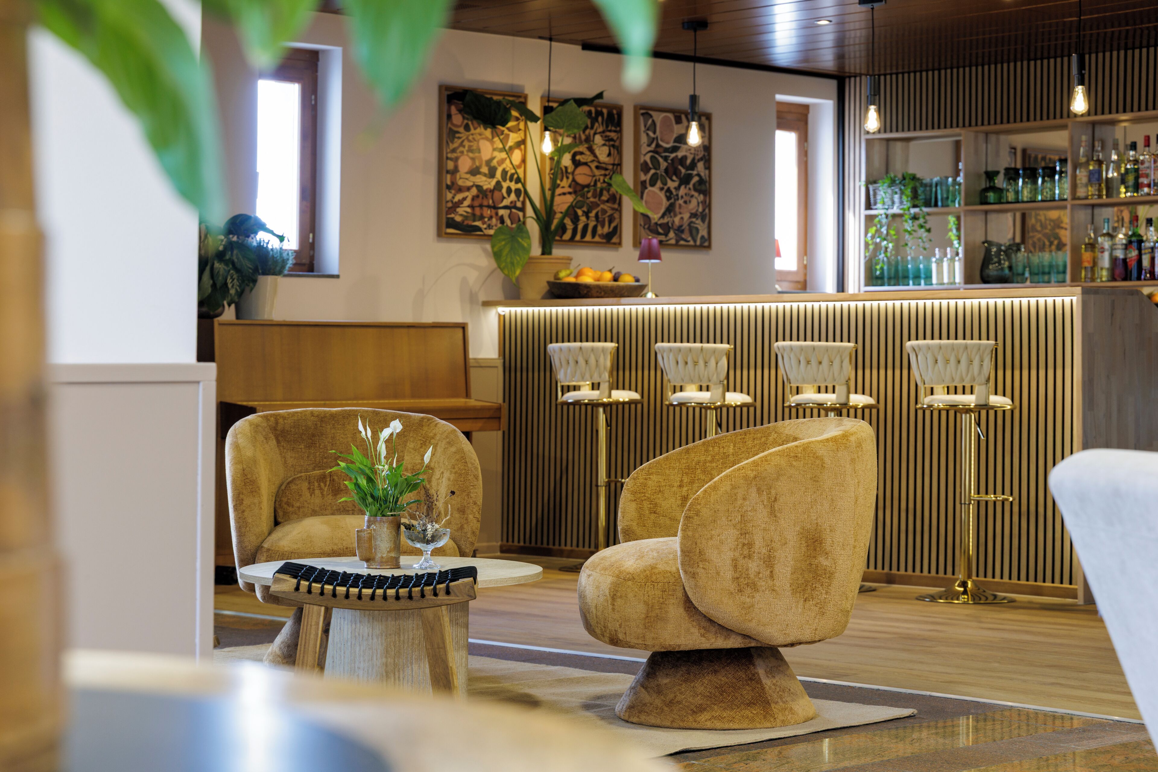 Un interior moderno con una zona de bar, asientos con una mesa redonda y plantas decorativas.