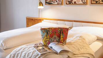 Un lit bien fait, agrémenté d’un coussin coloré, d’un magazine et d’une paire de lunettes posés sur le lit.