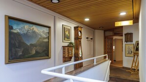 A staircase with a white handrail, a painting of a mountain landscape, a clock, and a framed picture on the wall.