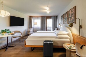 Habitación de hotel con cama, escritorio, silla, maleta y televisor.