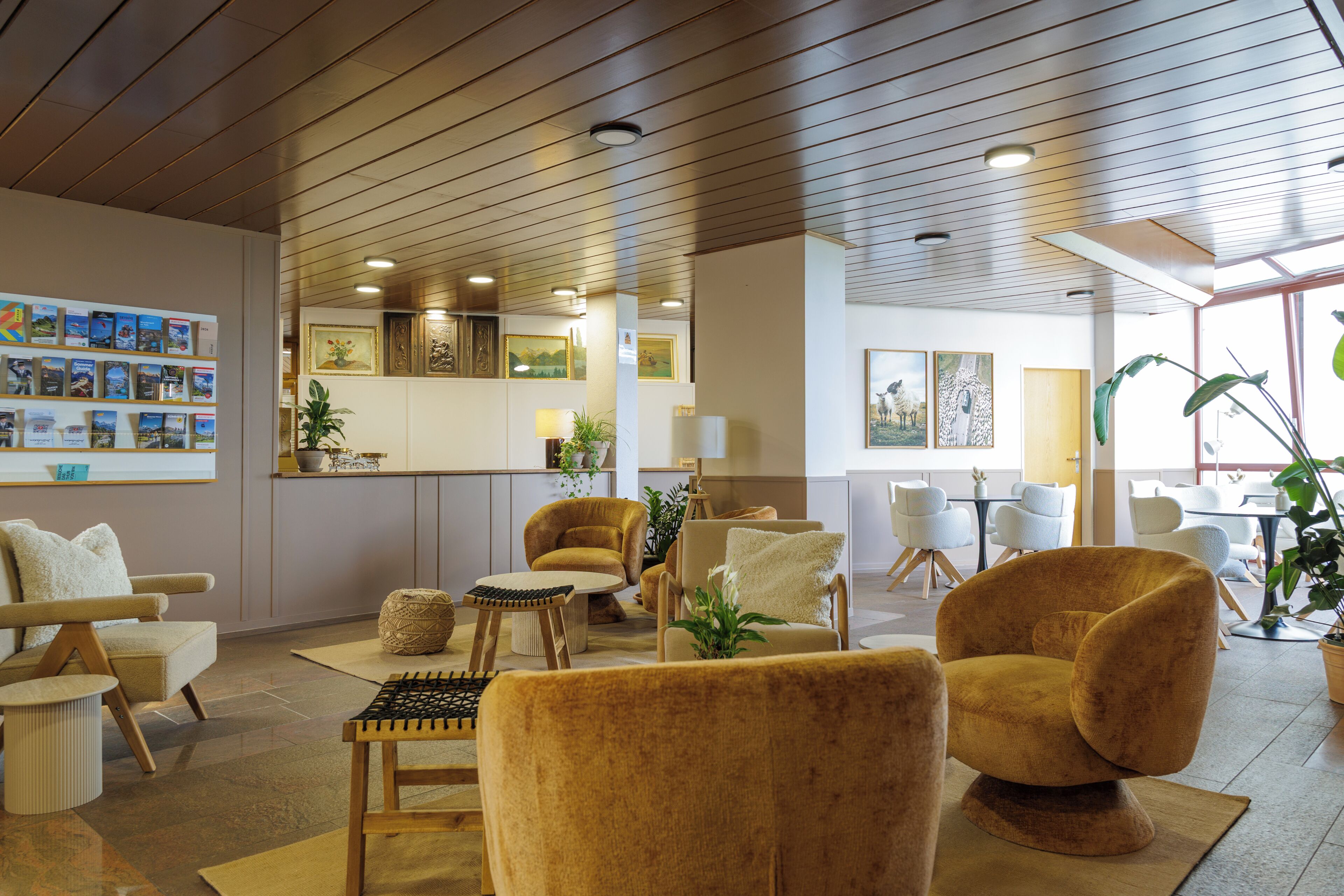 A modern hotel lobby with a wooden ceiling, comfortable seating, a reception desk, and artwork on the walls.