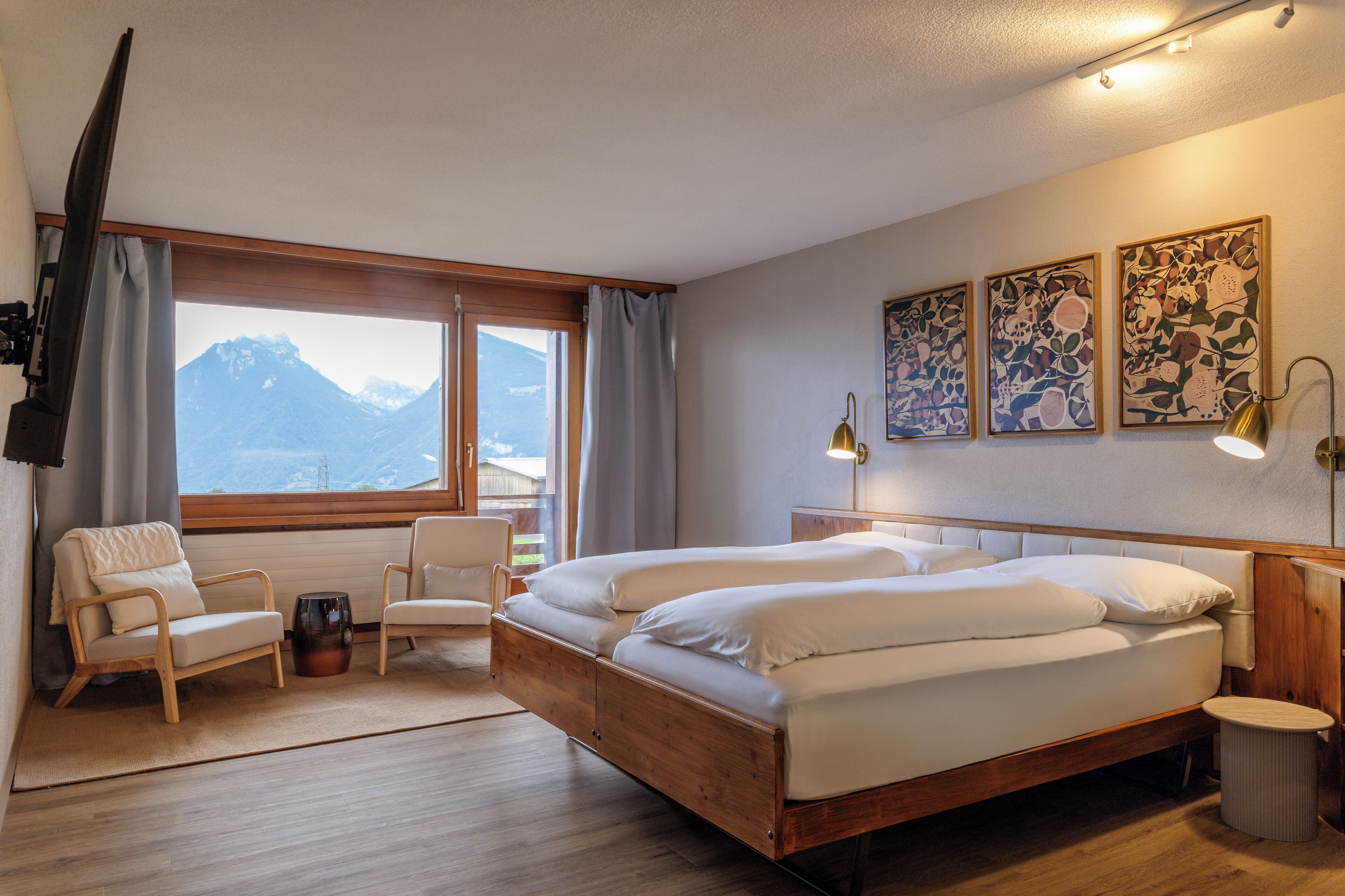 Ein Hotelzimmer mit Bett, zwei Stühlen, einem kleinen Tisch, einer Lampe und Bildern an der Wand.