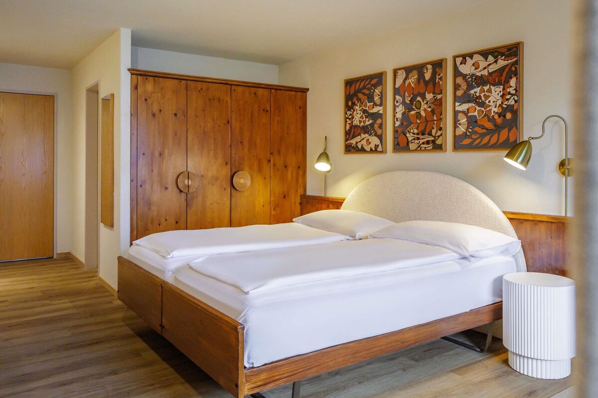 A bedroom with a wooden bed, a nightstand, a lamp, and two wall art pieces.