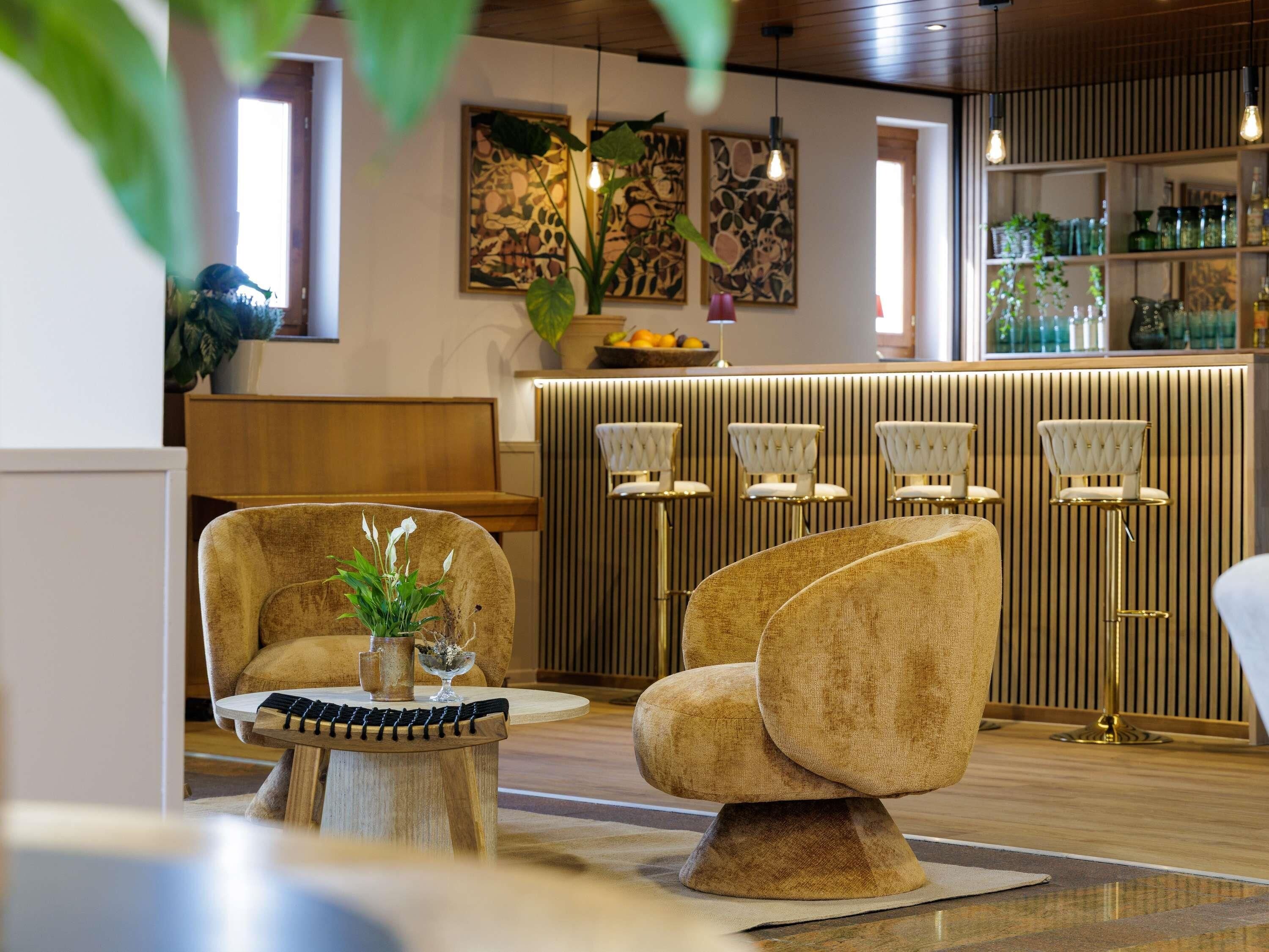 Een modern interieur met een zithoek, bestaande uit een ronde tafel en twee fauteuils, een houten kast met glazen en een muur met abstracte kunst.