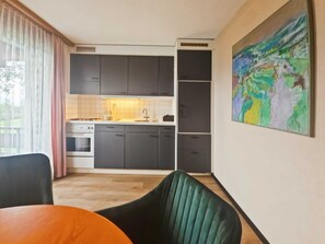 Une cuisine moderne avec des meubles de couleur sombre, un plan de travail blanc et une grande fenêtre ornée de rideaux légers.