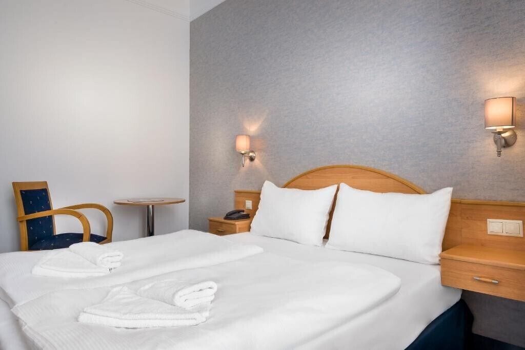 Habitación de hotel con una cama grande, dos mesitas de noche, una silla y una pequeña mesa.