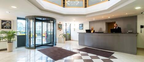 A hotel lobby with a check-in counter, a glass door entrance, and a modern interior design.