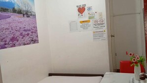 A small room with a bed, a table with a vase, and a wall with various notices. - WJV INN MANDAUE CENTRO (Mandaue)
