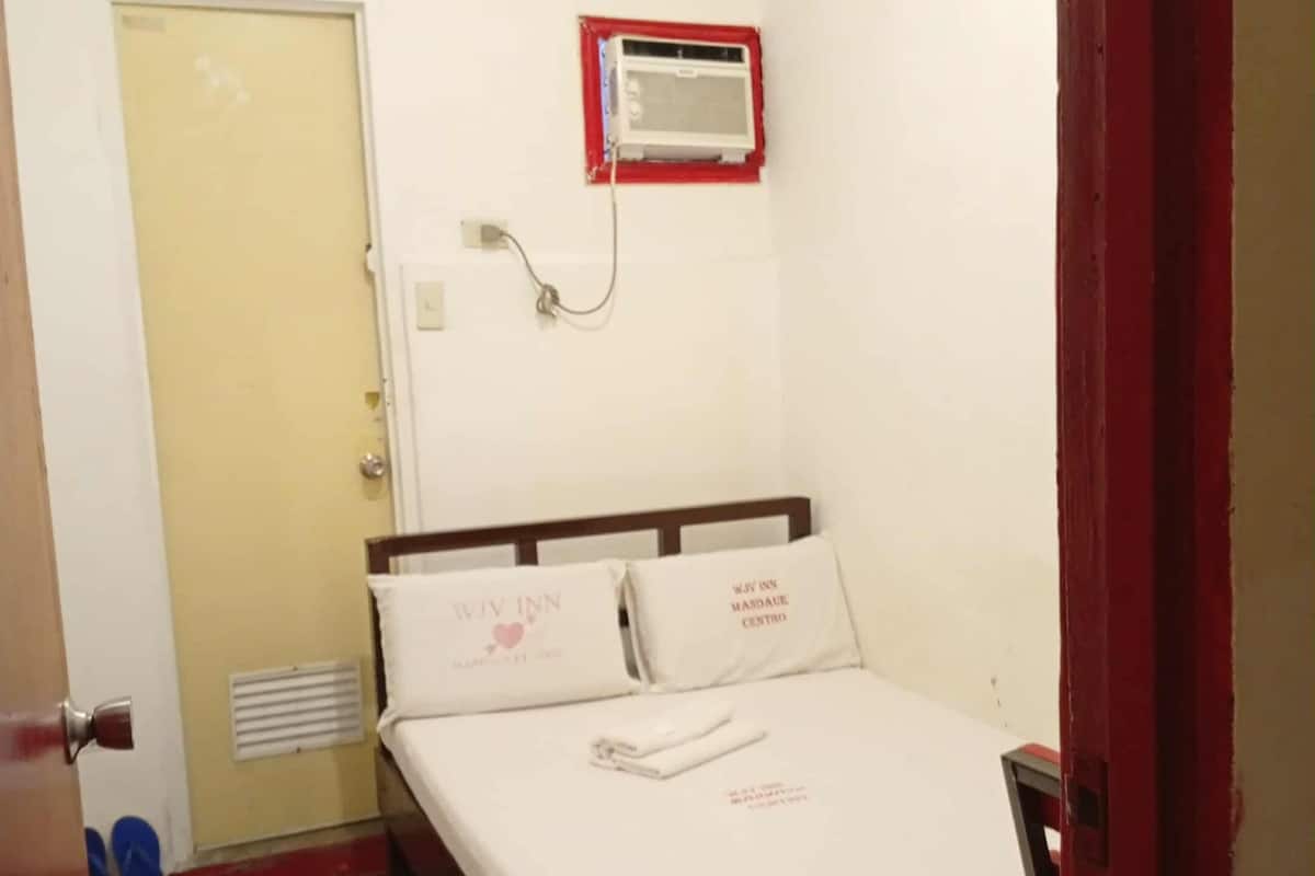 Una habitación de hotel con una cama, una puerta, una rejilla de ventilación y un aire acondicionado montado en la pared.