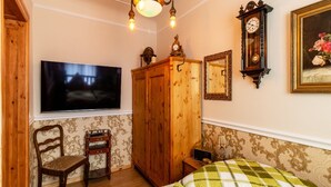 Ein Schlafzimmer mit einem Bett, einem Holzschrank, einem Fernseher, einer Uhr und einem gerahmten Bild an der Wand.
