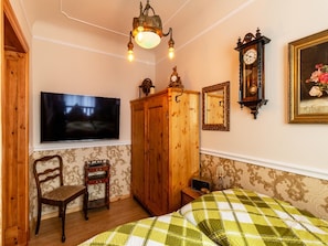 A bedroom with a bed, a wooden wardrobe, a television, a clock, and a framed picture on the wall. - Holiday Apartment Antik, 34 sqm, 1 Bedroom, max. 3 Persons (Potsdam)