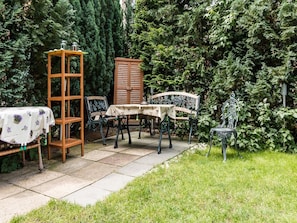 Une terrasse de jardin avec une table, des chaises, un buffet en bois et un banc en métal.
