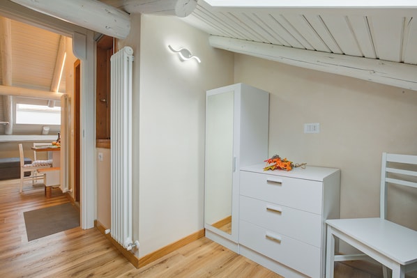A room with a wooden floor, white furniture, a radiator, and a window with a light fixture. - Caterina View (Livigno)