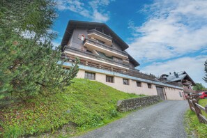 Un immeuble à plusieurs étages doté de balcons, d’un mur en pierre et d’un chemin de gravier menant à l’entrée.