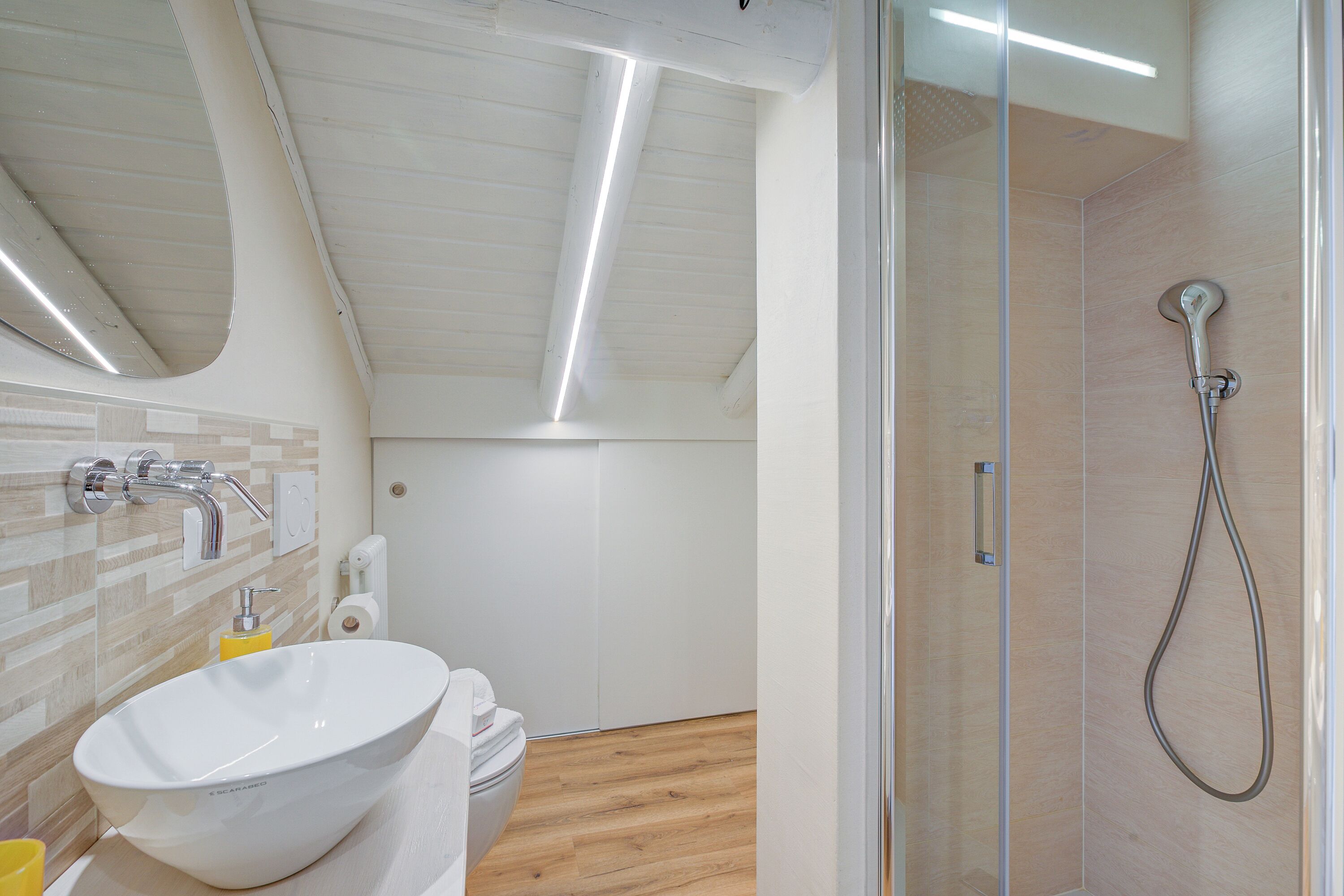 A modern bathroom with a large white sink, a glass shower enclosure, and a wooden floor.