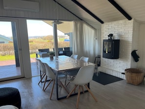 Uma área de refeições com uma mesa e cadeiras, uma televisão fixada em uma parede de tijolos, e vista para o exterior.