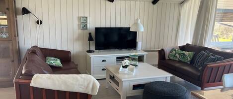 A living room with a brown sofa, a white coffee table, a black ottoman, a television, and a white cabinet.