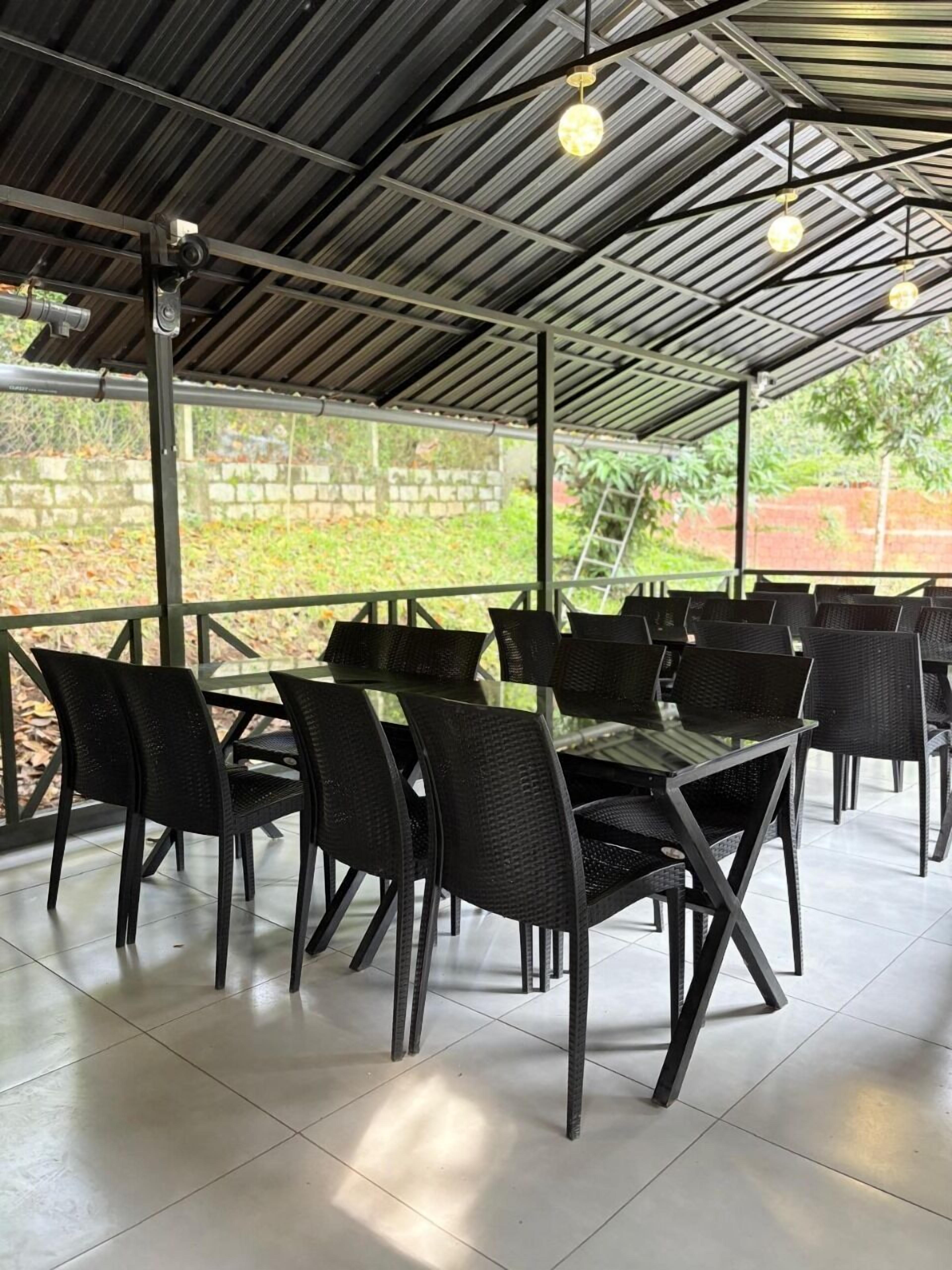 An outdoor dining area with a covered roof, metal beams, and black wicker chairs and tables.