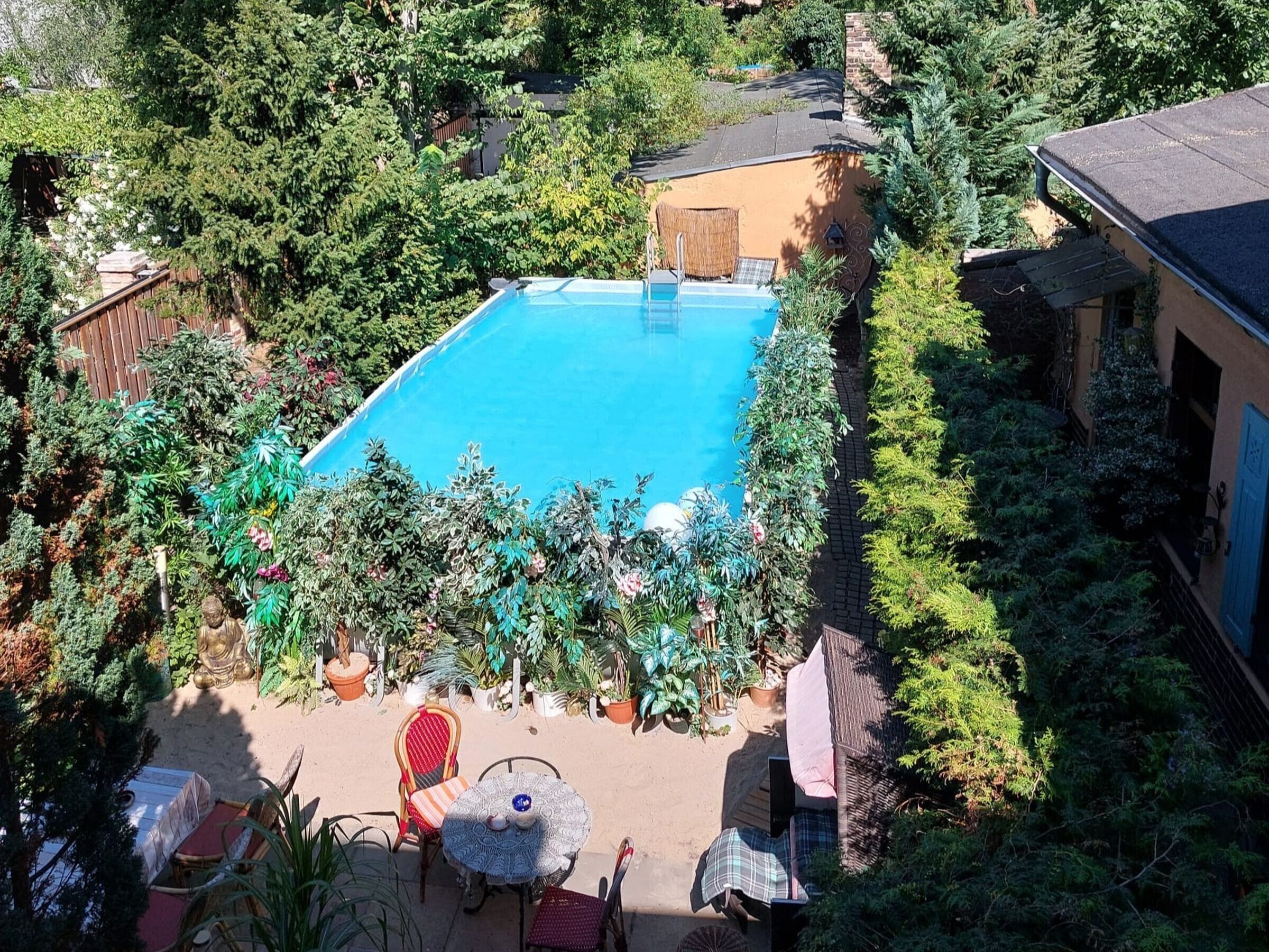 Una piscina rodeada de vegetación exuberante, una terraza de madera y un edificio con una puerta azul.
