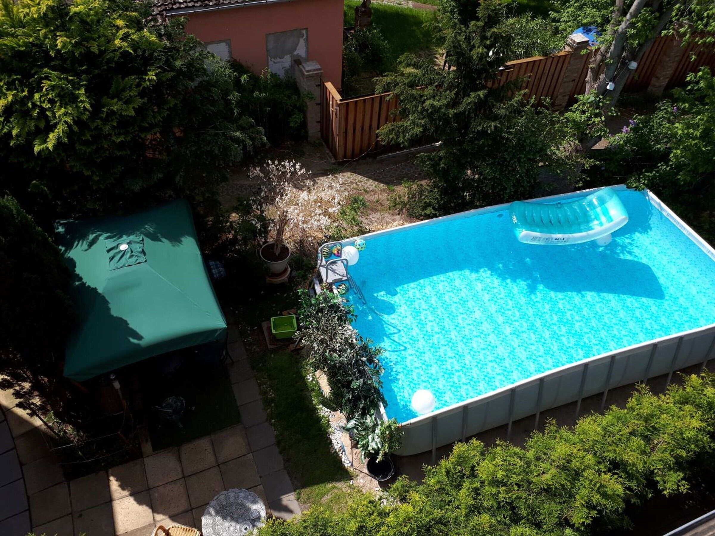 Piscina retangular com um assento flutuante, rodeada por uma cerca de madeira e vegetação exuberante.