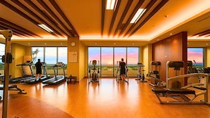 A spacious gym with treadmills, elliptical machines, and weight stations, featuring large windows with a scenic view. - Sea Family Room in Front of US Embassy (Manila)