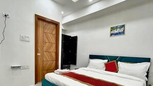 A bedroom with a bed, ceiling fan, recessed lighting, a door, and a wall-mounted artwork. - Roomshala Hotel J JOy (New Delhi)