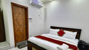 A bedroom with a bed, a ceiling fan, an air conditioning unit, and a wooden door. - Roomshala Hotel J JOy (New Delhi)