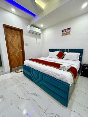 A bedroom with a bed, a wooden door, an air conditioning unit, and a wall-mounted artwork. - Roomshala Hotel J JOy (New Delhi)