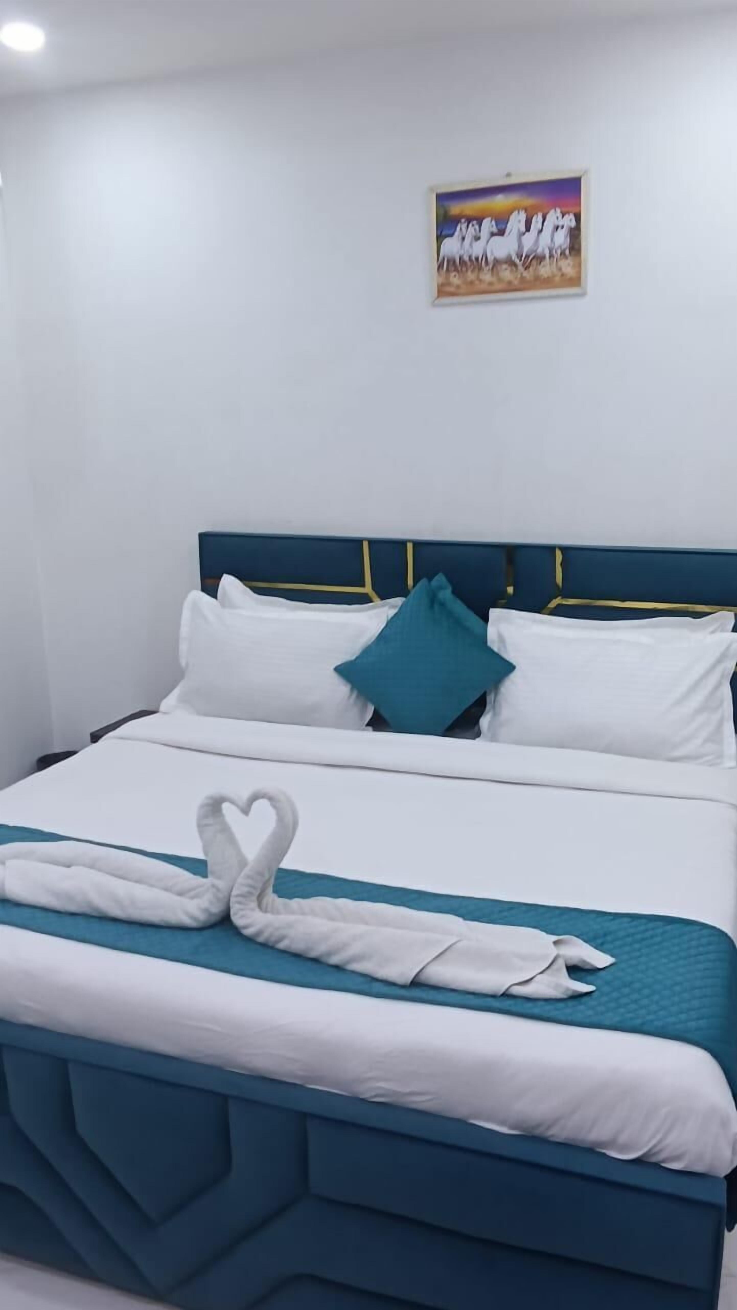 Un letto rifatto con cura, con biancheria da letto bianca e color acquamarina, un cuscino color acquamarina e un'accattivante disposizione di asciugamani a forma di cuore.
