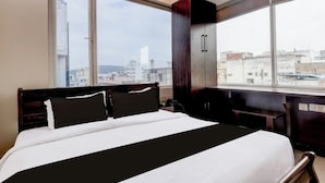 A hotel room with a large bed, a view of the city through large windows, and a cityscape visible outside. - SRI ADITI INN (Vijayawada)