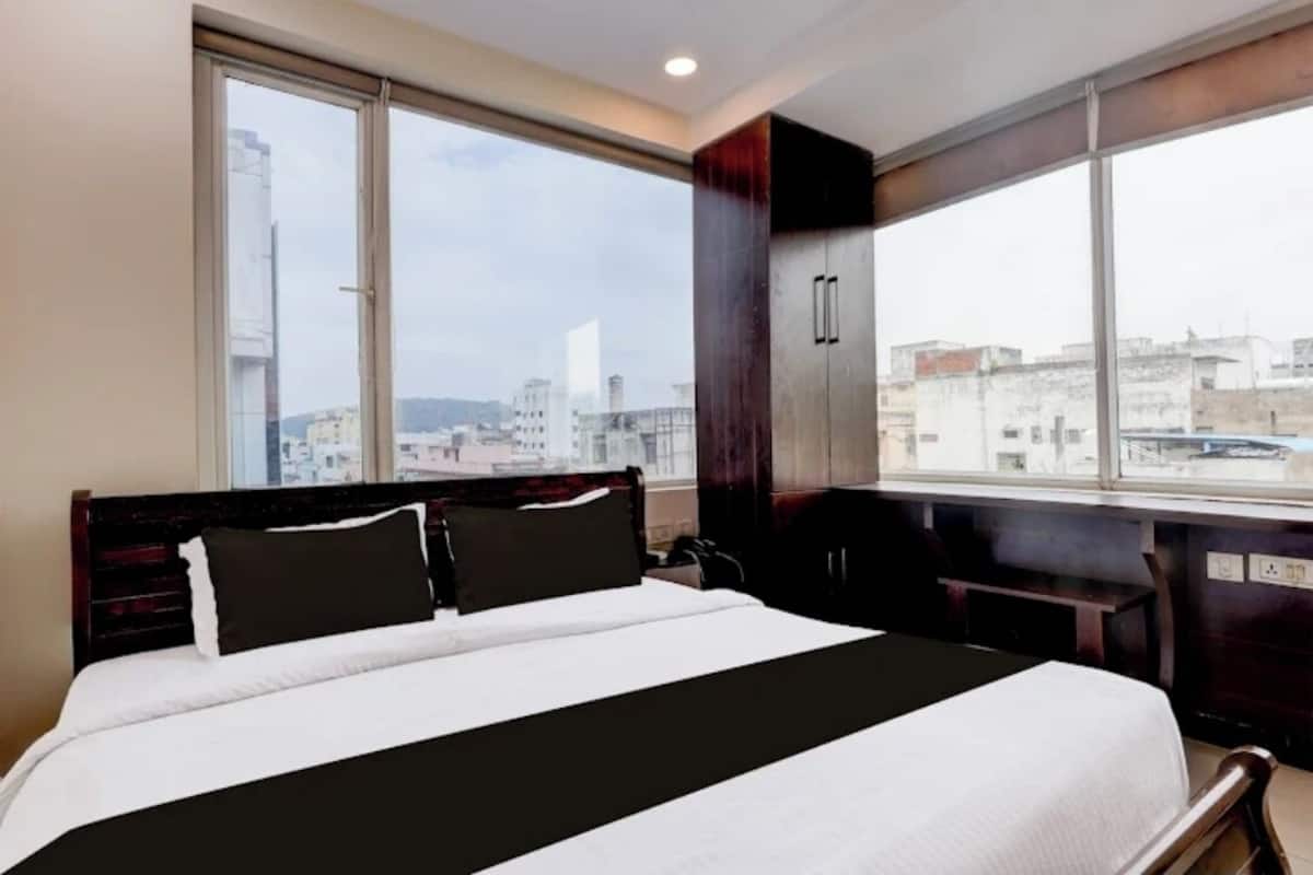 A hotel room with a large bed, a view of the city through a window, and a wardrobe.