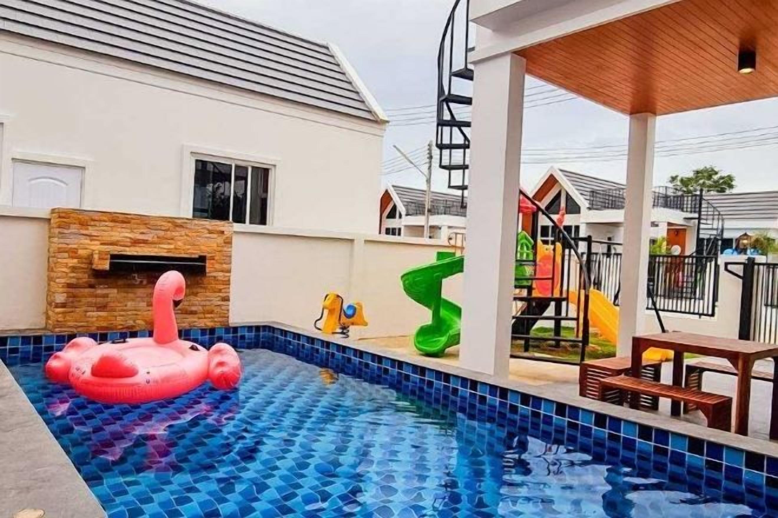 A swimming pool with a pink inflatable float, a children's play area with slides, and a covered seating area.
