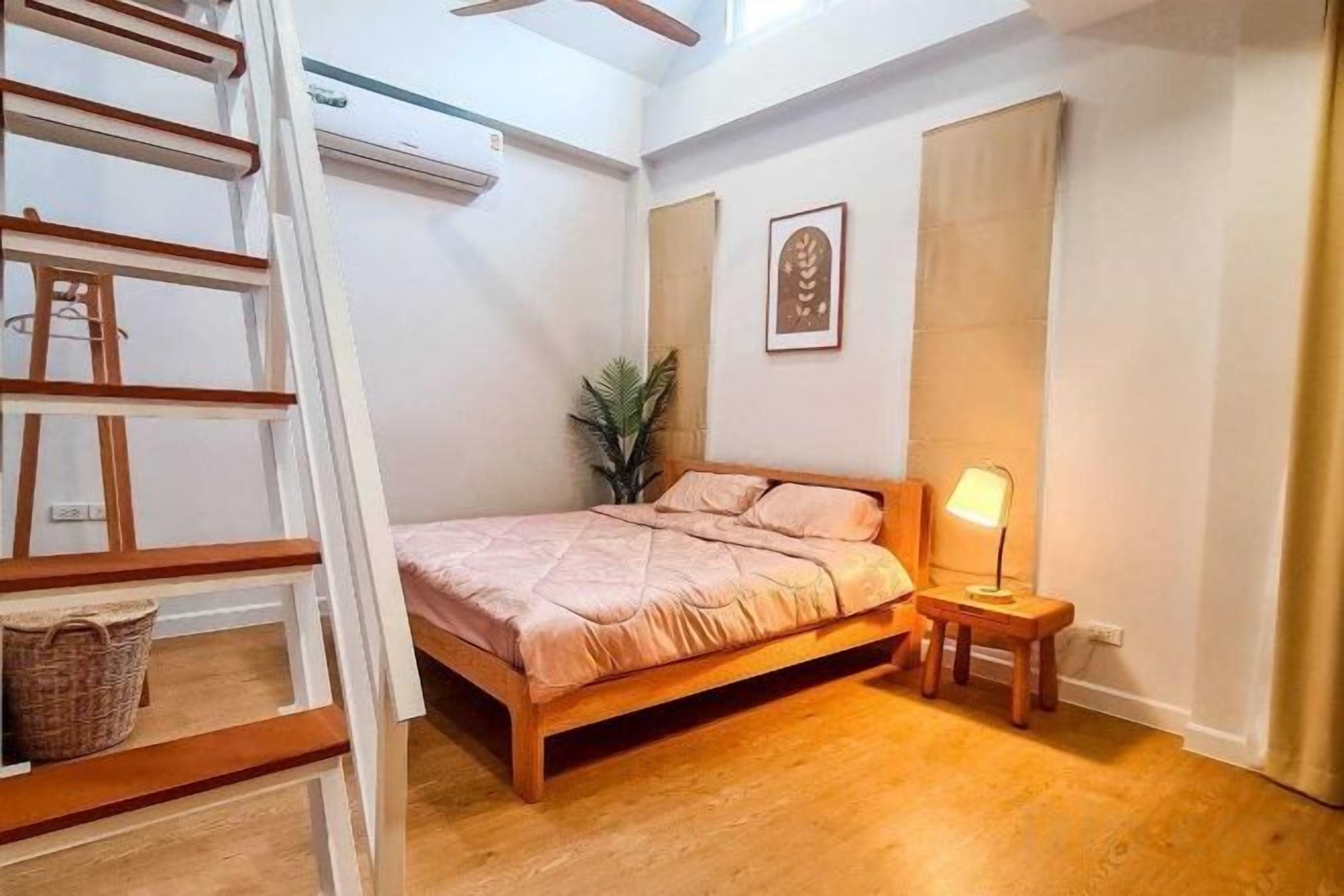 A bedroom with a bed, bedside table, lamp, and a wooden ladder.