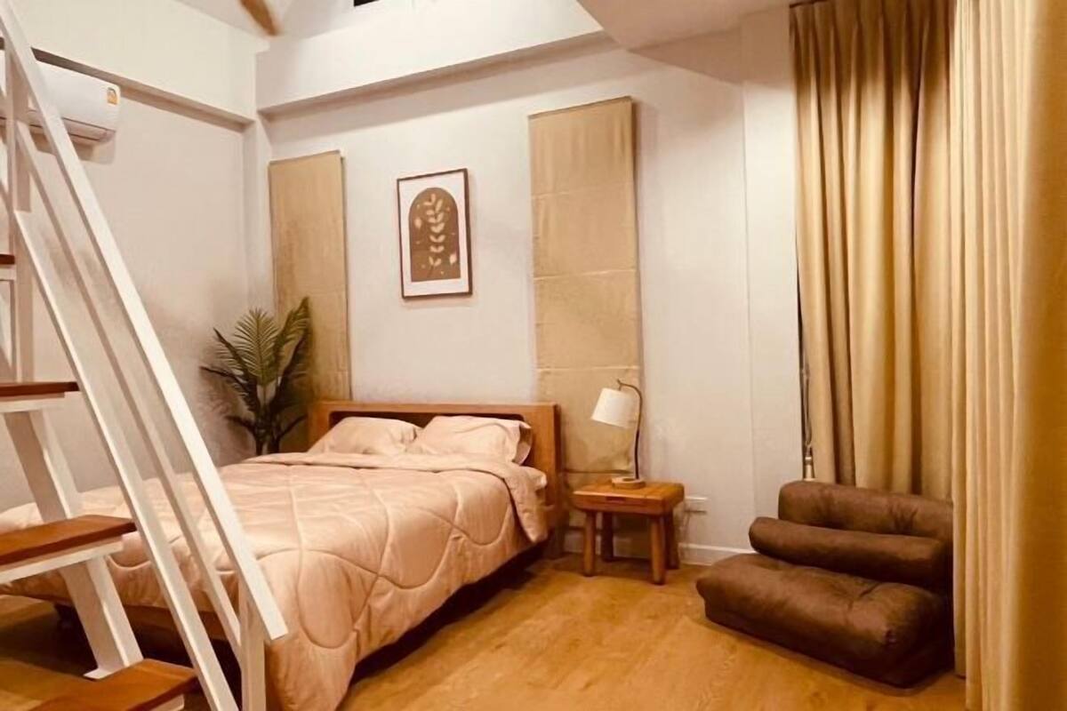 A bedroom with a bed, a nightstand, a lamp, a chair, and a staircase.