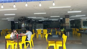 A dining area with yellow chairs and tables, a ceiling fan, and a sign indicating a smoking area. - Tomato Motel (Langkawi)