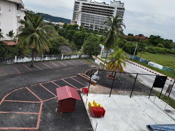 A parking area with marked spaces, a small red structure, and a road with traffic. - Tomato Motel (Langkawi)