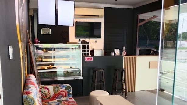 A modern interior with a sofa, a counter, stools, and a glass partition. - Tomato Motel (Langkawi)