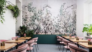 Un restaurante con mostrador verde, sillas rosas y un mural floral en la pared.