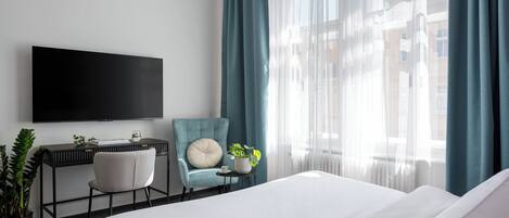 Une chambre d’hôtel avec un lit, un bureau et une chaise, une télévision et une fenêtre avec des rideaux.