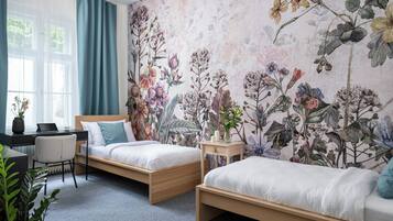 A bedroom with two beds, a desk, and a large floral mural on the wall.