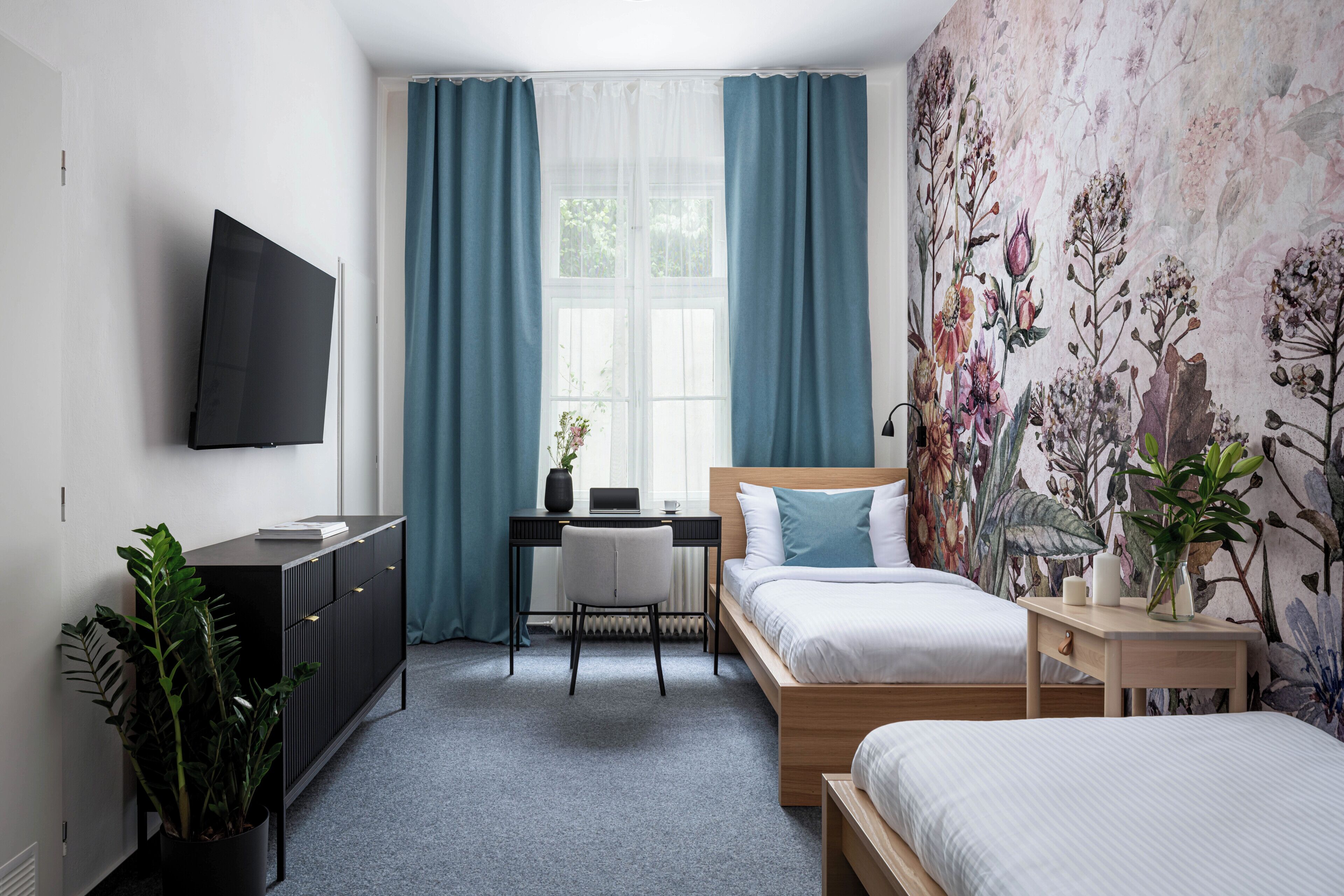 A bedroom with a bed, a desk, a TV, and a window with curtains.