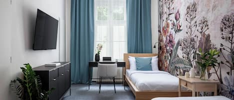 Un dormitorio con cama, escritorio, televisor y ventana con cortinas.
